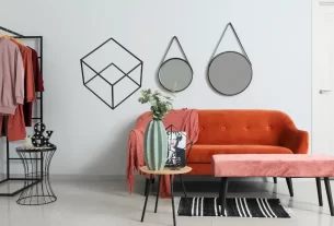 Ambiente de sala de estar claro e arejado, sem armários, com uma estante aberta e uma arara de roupas como parte da decoração.