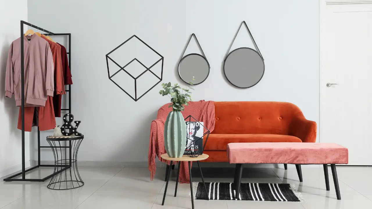 Ambiente de sala de estar claro e arejado, sem armários, com uma estante aberta e uma arara de roupas como parte da decoração.