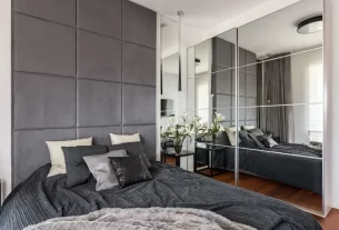 Quarto pequeno bem decorado com paredes claras, uma cama aconchegante e um espelho grande que amplia o espaço.