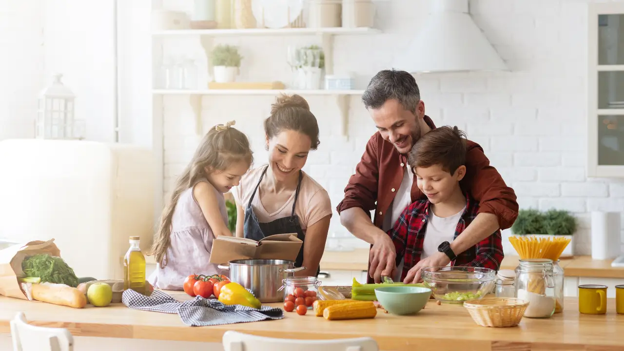 Uma família feliz cozinhando junta em uma cozinha com bancadas e gavetas visivelmente organizadas.