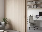 Parede deslizante de madeira clara em um ambiente pequeno e moderno, separando a área de estar de um escritório.